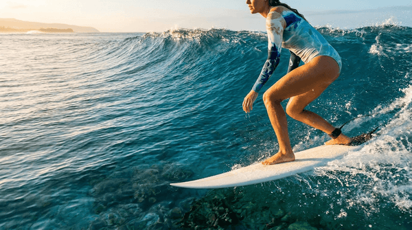 Surfeuse en combinaison surf manches longues UPF50+ sur une vague, eau turquoise — Couleurs Lagon