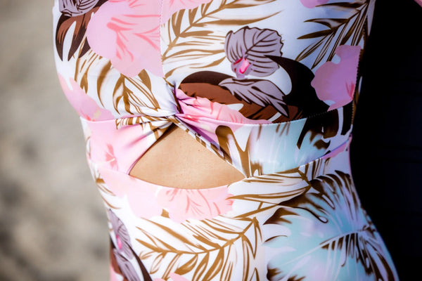 Détail du nœud torsadé, de la découpe triangulaire et de l'imprimé floral de la combi surf femme rose floral portée par Moea